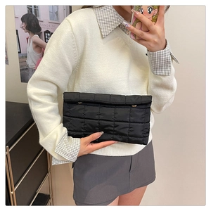 Detail of a black quilted puffer handbag featuring a flap cover and soft cotton texture