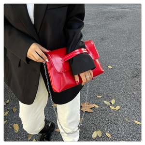 Close-up of vibrant red patent leather envelope bag held by model in street setting