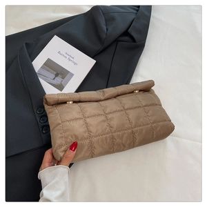 Close-up of brown quilted envelope clutch featuring luxury gold fasteners on white fabric