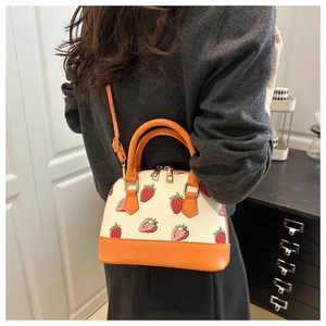 Detail of strawberry print crossbody shell bag with orange leather straps and handles