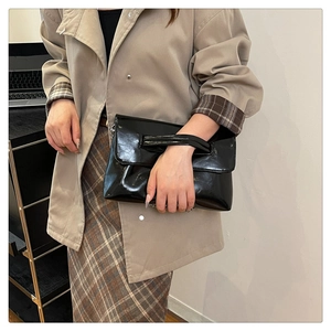 Detailed view of black glossy patent leather crossbody bag with chain strap and top handle