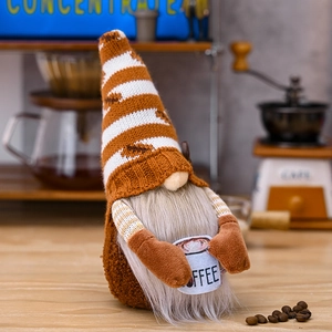 Close-up of a knitted coffee gnome holding a white cup on a table with coffee beans