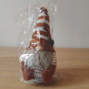 Close-up of coffee gnome plush with knitted hat holding a cup marked with COFFEE text