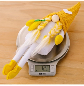 Lemon themed long legged knit gnome doll being weighed on a scale showing 129g weight