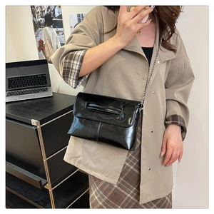 Close-up of a black glossy leather crossbody envelope bag with a fine metal chain strap