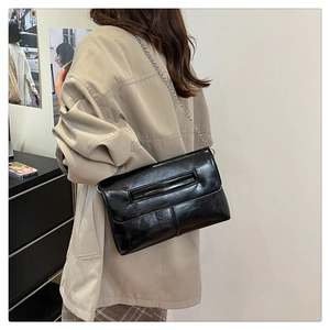 Detail shot of a black glossy patent leather crossbody bag with silver chain strap