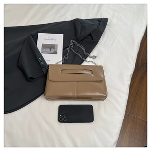 Detailed shot of brown glossy PU leather handbag with silver chain on white sheets