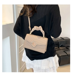 Detail of beige quilted bag with ruched handle and square metal lock shown on a model