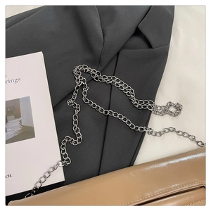 Detail of khaki leather clutch bag with silver chain strap on fashion magazine backdrop