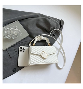 Close-up of quilted white crossbody bag with ruched handle and gold square buckle detail