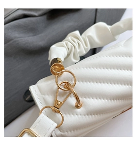 Detail of white quilted leather bag showing gold hardware and pleated shoulder strap