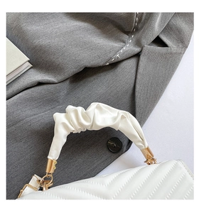 Detail view of white quilted crossbody bag featuring a unique scrunchie handle and gold rings