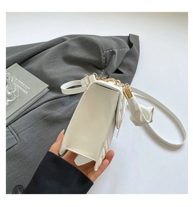 Detailed side view of white quilted crossbody bag with golden hardware and bow detail