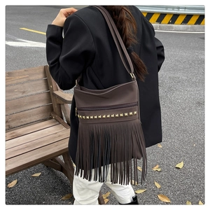 Detail of dark brown leather tote bag featuring gold pyramid studs and long fringe tassels
