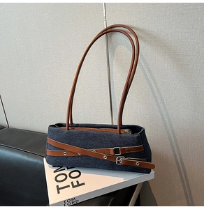 Detailed view of dark blue denim shoulder bag featuring brown leather straps and metal buckles