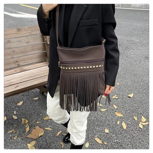 Brown tassel crossbody bag with gold studs shown in a stylish outdoor autumn street setting