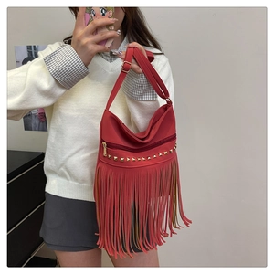 Detail view of red PU leather tote bag featuring gold pyramid studs and bohemian tassels