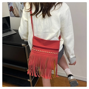Detail of red tassel shoulder bag featuring gold square rivets and bohemian fringe style