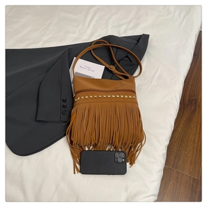 Close-up of brown PU leather shoulder bag with golden studs and bohemian fringe details