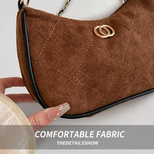 Close-up of brown suede shoulder bag with quilted texture and gold metal ring buckle
