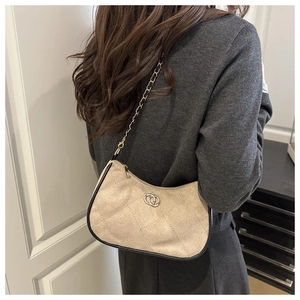 Quilted crossbody bag with gold chain strap worn over a grey sweater and black skirt