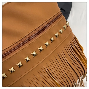 Detail of brown leather tote showing gold square rivets, fringe trim, and zip closure