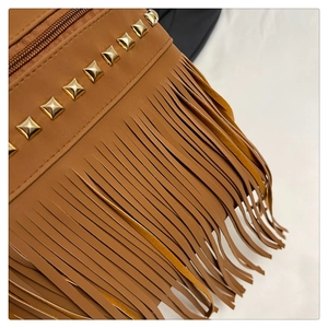 Close-up of golden studs and long fringe details on brown faux leather hobo bag
