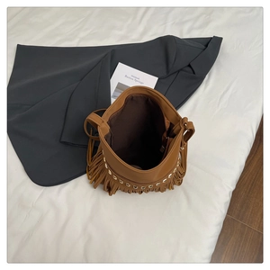 Detail view of brown leather bucket bag featuring gold rivets and long fringe tassels