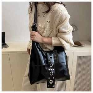 Close-up of black glossy leather handbag with large metal eyelet grommet strap detail