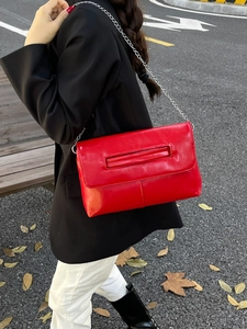 Fashionable red leather crossbody bag with metal chain strap shown on street scene