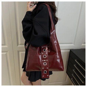 Close-up of burgundy glossy leather bag with metal grommets and industrial rivets