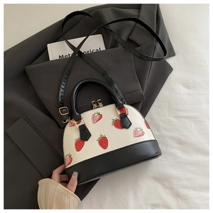 Detail of shell handbag featuring strawberry prints, color-block design, and gold zippers