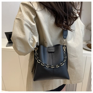 Detail of black pebbled leather bucket bag featuring decorative chain and printed strap