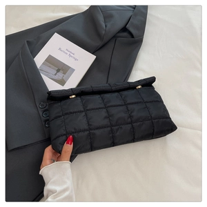 Detail of black quilted puffer envelope bag with gold round metal buckle and nylon texture