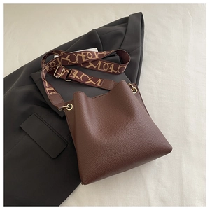 Detail of dark brown pebble leather bucket bag with gold ring and patterned wide strap