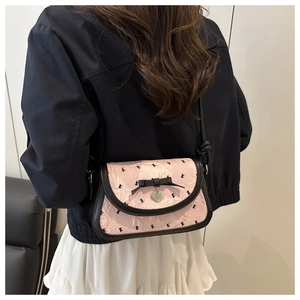 Détail du sac bandoulière en jacquard rose avec pendentif cœur et nœud sur la hanche