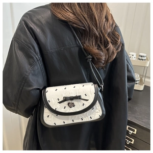 Detail of a textured white crossbody bag with black trim and a heart pendant accent