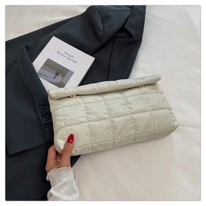 Close-up of beige quilted envelope clutch with gold metal details on grey blazer background