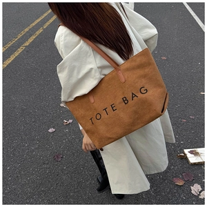 Gros plan d'un sac cabas en daim marron avec imprimé TOTE BAG porté à l'épaule dehors