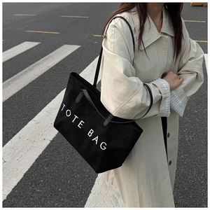 Gros plan d'un sac cabas noir minimaliste avec texte TOTE BAG porté par un mannequin en ville
