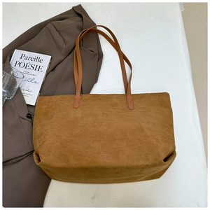 Gros plan du sac cabas en daim caramel avec fines anses sur un bureau blanc minimaliste
