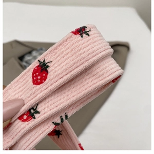Nahaufnahme der rosa Cord-Textur und der roten Erdbeerstickerei auf der Umhängetasche