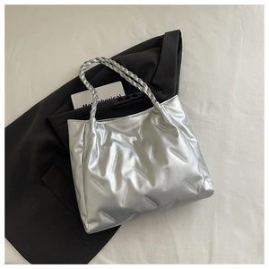 Detail of silver tote bag with diagonal quilting and woven handles on a gray suit