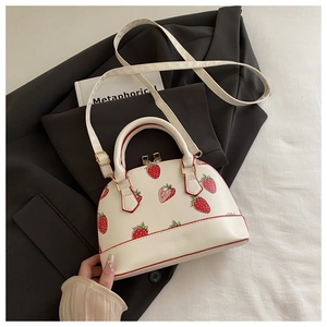 Close-up of white shell bag with strawberry print and gold hardware on a suit jacket