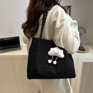 Detail of black pleated tote bag with woven straps and a white cloud charm accessory
