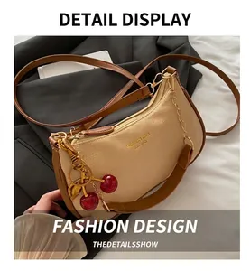 Close-up of cream textured leather bag with cherry charm and gold chain details