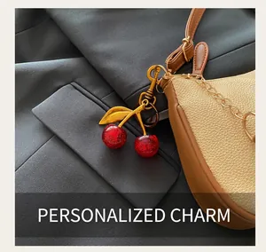 Detailed view of red glitter cherry charm with gold leaves on a brown leather bag