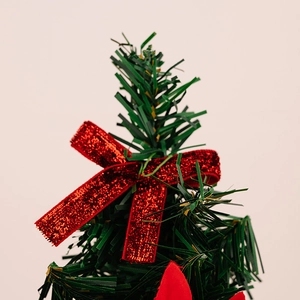 Close-up of a mini Christmas tree top with a glittering red bow on green pine branches