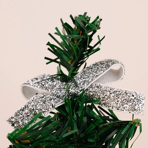 Close-up of a silver glitter bow decoration on green artificial Christmas tree branches