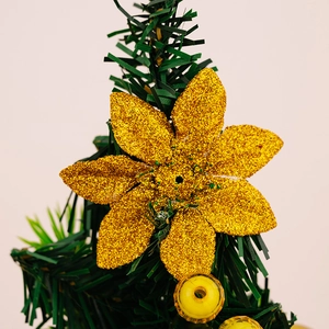 Close-up of golden glitter flower ornament hanging on a decorative mini Christmas tree